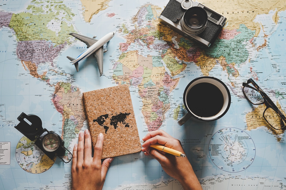 Top view of young woman planning her vacation using world map - Travel influencer looking for the next travel destination - Concept of adventure, tourism, and traveling people lifestyle